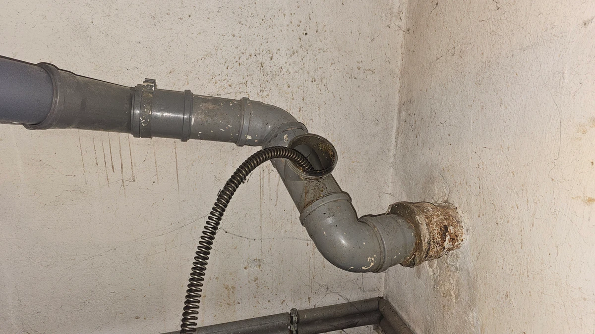 Spirala sprężyny elektrycznej wprowadzona przez otwartą rewizję rury kanalizacyjnej w piwnicy — udrożnienie odpływu do szamba