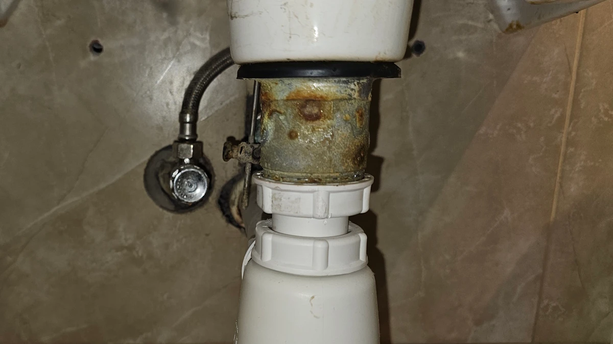 Podrdzewiały metalowy korpus spustu umywalki nad syfonem przed wymianą